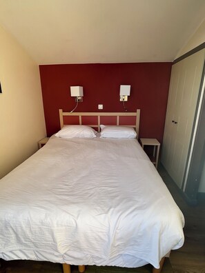 A single bed with a wooden headboard, two bedside tables, and a red accent wall. - Duplex in vacation village SEA (Saint-Raphaël)