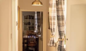 A hallway with a door, a hanging light fixture, and a window with curtains.