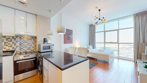 Een moderne keuken met een fornuis, magnetron en wasmachine, een eethoek met een tafel en stoelen, en een groot raam met uitzicht.