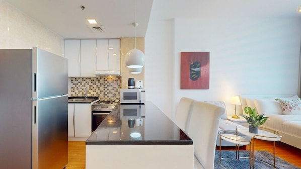 A modern kitchen with a central island, a dining area with a white sofa and chairs, and a living room with a couch and a painting. - Bright and Spacious Studio in JVT l Free Pool,Gym (Jumeirah Village Triangle)
