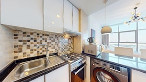 A modern kitchen with a tiled backsplash, stainless steel appliances, and a view through the window. - Bright and Spacious Studio in JVT l Free Pool,Gym (Jumeirah Village Triangle)