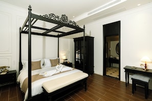 A four-poster bed with a canopy, a bedside table with a lamp, a mirror, and a dark wooden cabinet.