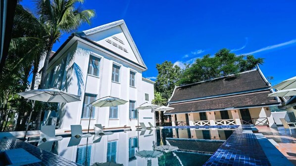 A pool area with a reflection of a building, palm trees, and umbrellas. - Jing Land Palace Hotel Luang Prabang (Luang Prabang)