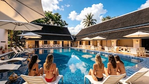 A swimming pool with lounge chairs and umbrellas, surrounded by a building with a tiled roof.