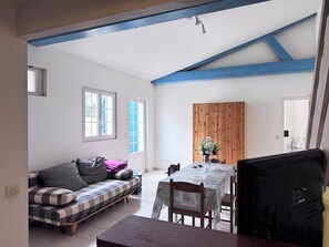 Ein Zimmer mit einer Couch, einem Esstisch mit Stühlen, einem Holzschrank und einer Decke mit blauen Balken.