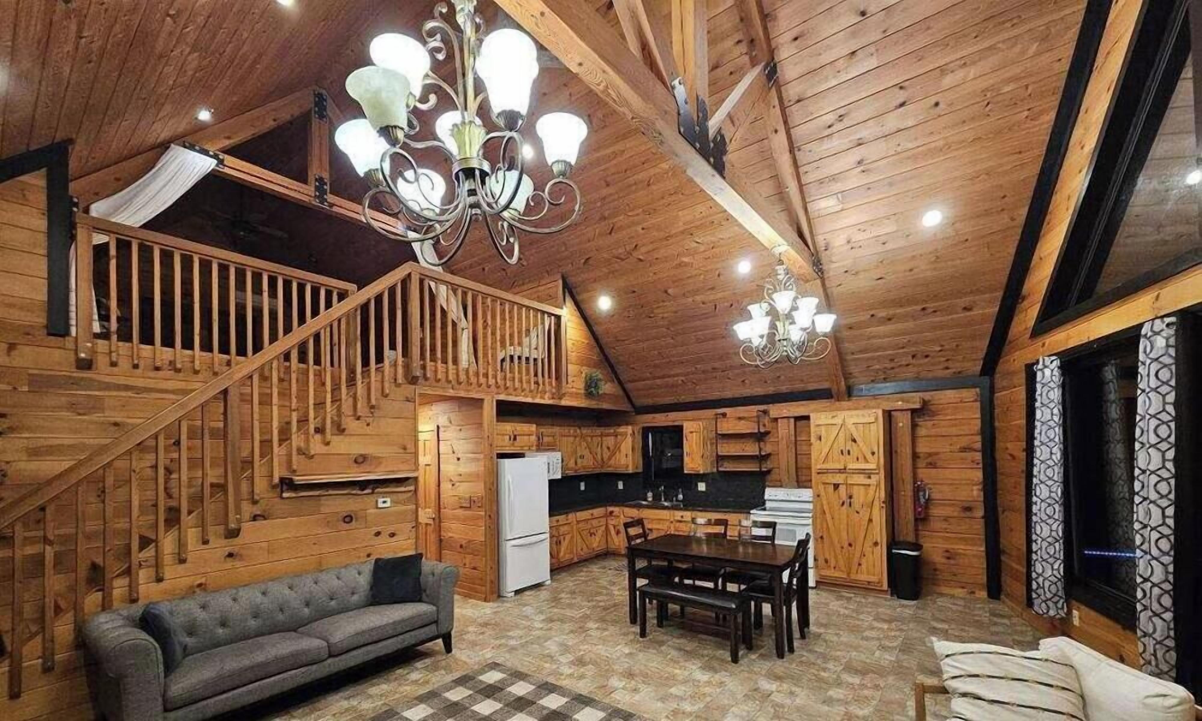 A wooden cabin interior with a staircase, kitchen, dining area, and a sofa.