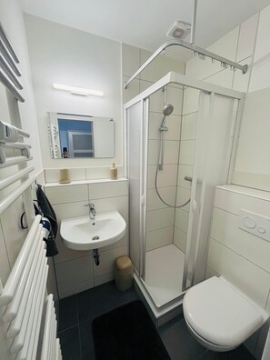 Een badkamer met een wit wastafel, spiegel, toilet, douchecabine en een handdoekrek.