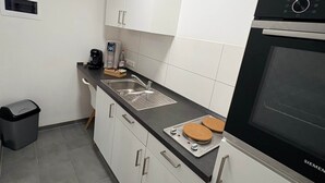 Moderni keittiö, jossa on valkoiset kaapit, musta uuni ja kahvinkeitin.