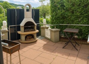 Une terrasse extérieure avec un four à pizza en pierre, un barbecue et une petite table.