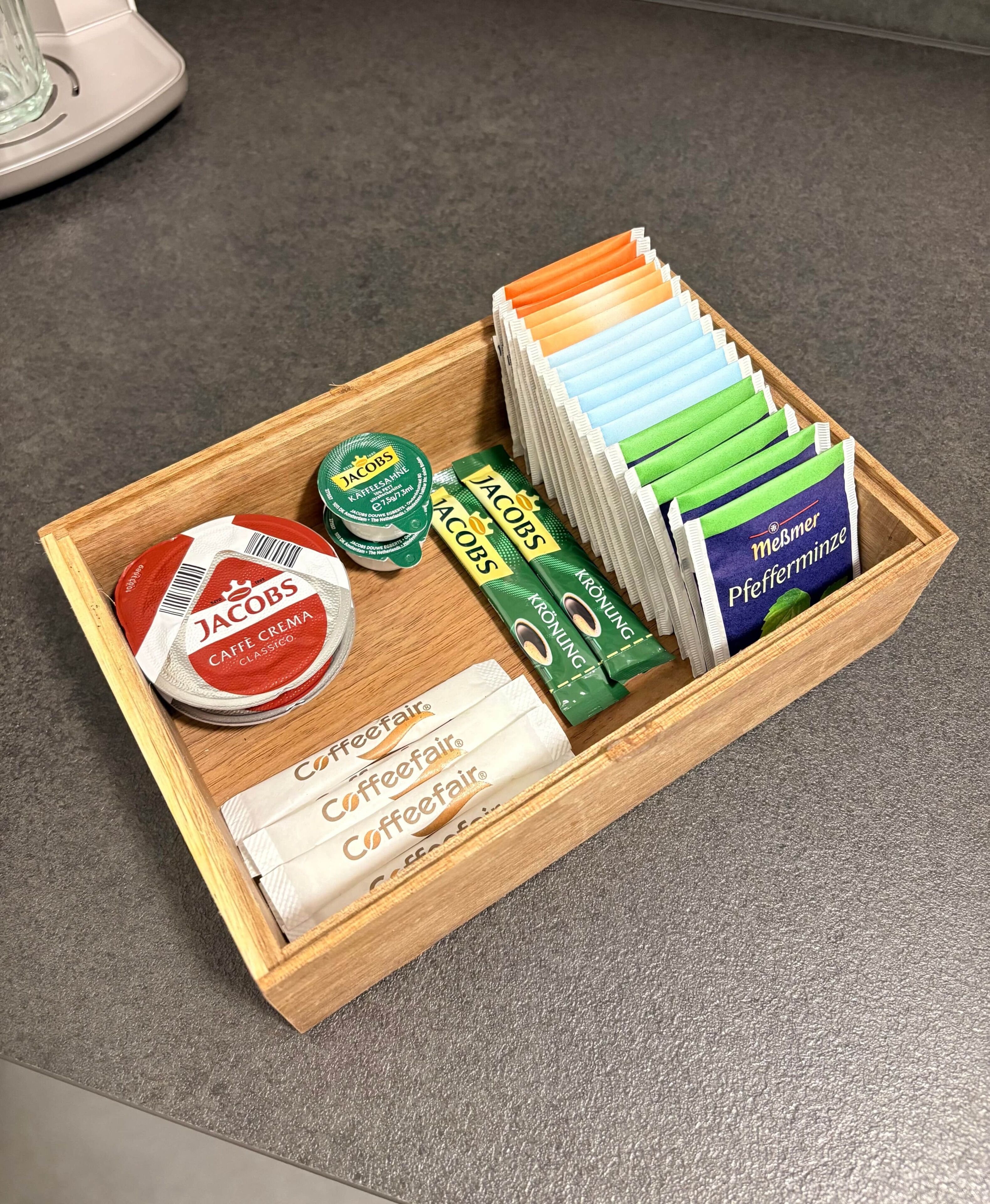 Ein Holztablett mit Kaffeefrahm, Kaffeekapseln und Kaffeebohnen.
