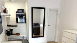 A compact living space with a kitchenette, a dining area, a sofa, and a mirror. - Sanssouci Holiday Apartment 13 (Bad Kissingen)