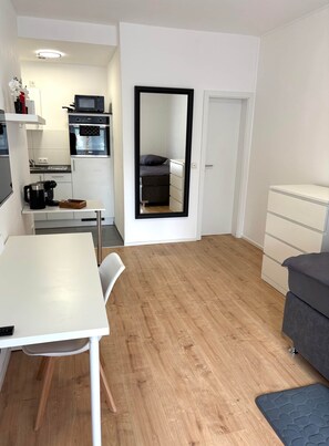 A compact living space with a kitchenette, a dining area, a sofa, and a mirror. - Sanssouci Holiday Apartment 13 (Bad Kissingen)