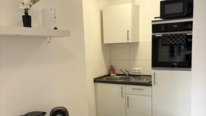A compact kitchen with a microwave, oven, and a coffee maker on the counter. - Sanssouci Holiday Apartment 13 (Bad Kissingen)