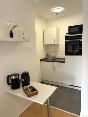 A compact kitchen with a microwave, oven, and a coffee maker on the counter. - Sanssouci Holiday Apartment 13 (Bad Kissingen)