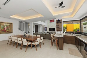 A modern kitchen with a built-in oven, a dining area with a wooden table and chairs, and a living room with a sofa and a TV. - Luxury Villa w/ Pier and Beach, Resort Amenities (Cozumel)