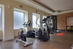 Ein Fitnessstudio mit verschiedenen Trainingsgeräten, großen Fenstern und einer Backsteinwand.