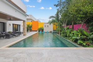 A modern outdoor pool area with a clear sky, surrounded by greenery and a variety of seating arrangements. - Luxury Villa w/ Pier and Beach, Resort Amenities (Cozumel)