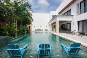A modern pool area with three Adirondack chairs, a covered seating area, and a clear view of the pool. - Luxury Villa w/ Pier and Beach, Resort Amenities (Cozumel)