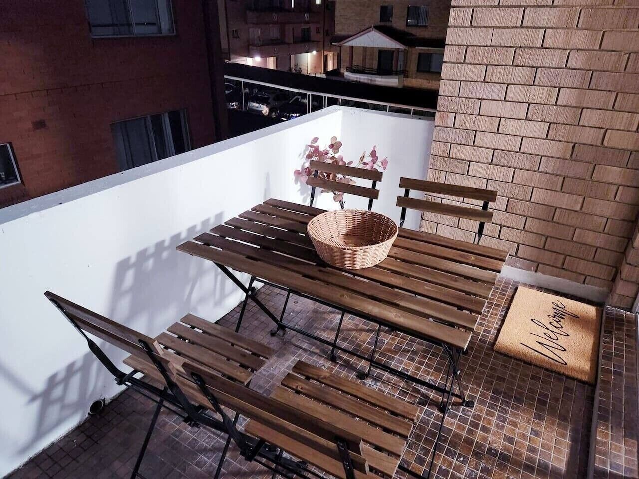 Un balcon avec une table et des chaises en bois, un panier en osier et un paillasson.