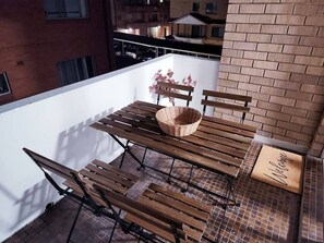 Un balcon avec une table et des chaises en bois, un panier en osier et un paillasson.