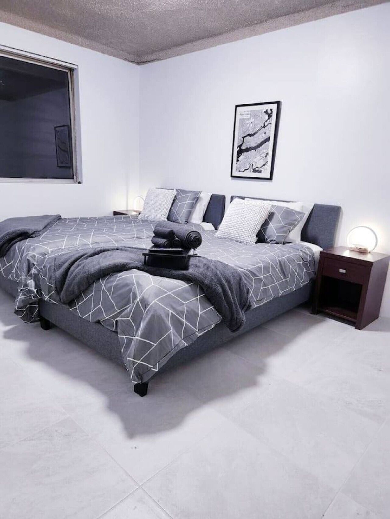 Un dormitorio moderno con una cama grande, una mesita de noche con lámpara y un cuadro enmarcado en la pared.