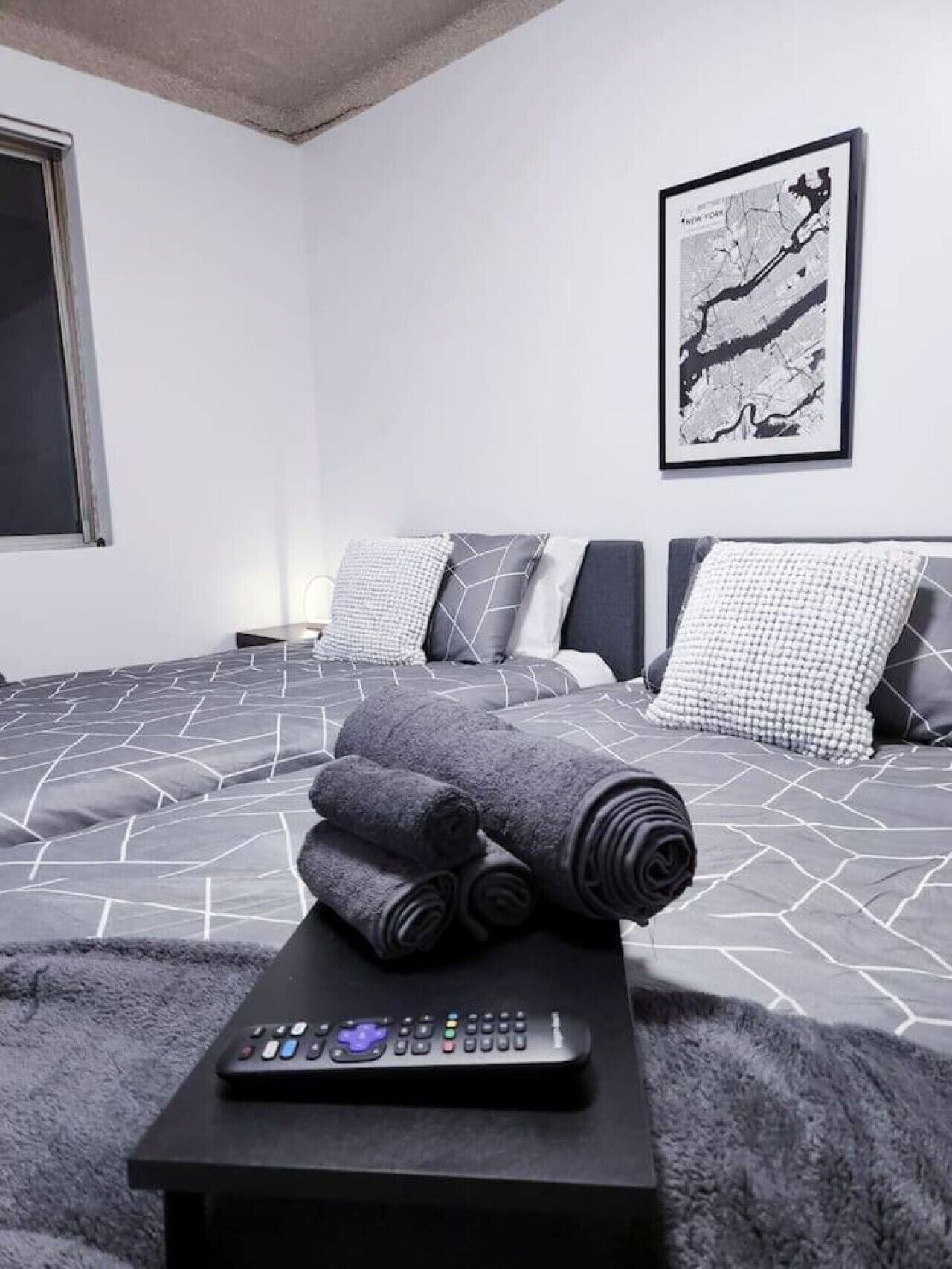 Une chambre à coucher moderne avec un lit, des oreillers, une carte accrochée au mur et une télécommande posée sur une table.