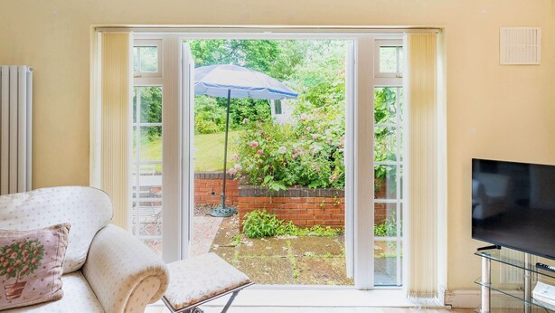 A room with a sofa, a television, and a sliding glass door leading to a garden. - 2 bed Bungalow in Towcester by ARP Homes, 15 min from Silverstone, Free Parking, Perfect for Families and Contractors (West Northamptonshire)