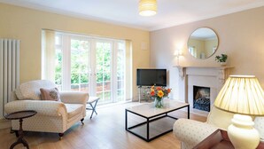 A living room with a sofa, a coffee table with flowers, a TV, and a fireplace. - 2 bed Bungalow in Towcester by ARP Homes, 15 min from Silverstone, Free Parking, Perfect for Families and Contractors (West Northamptonshire)