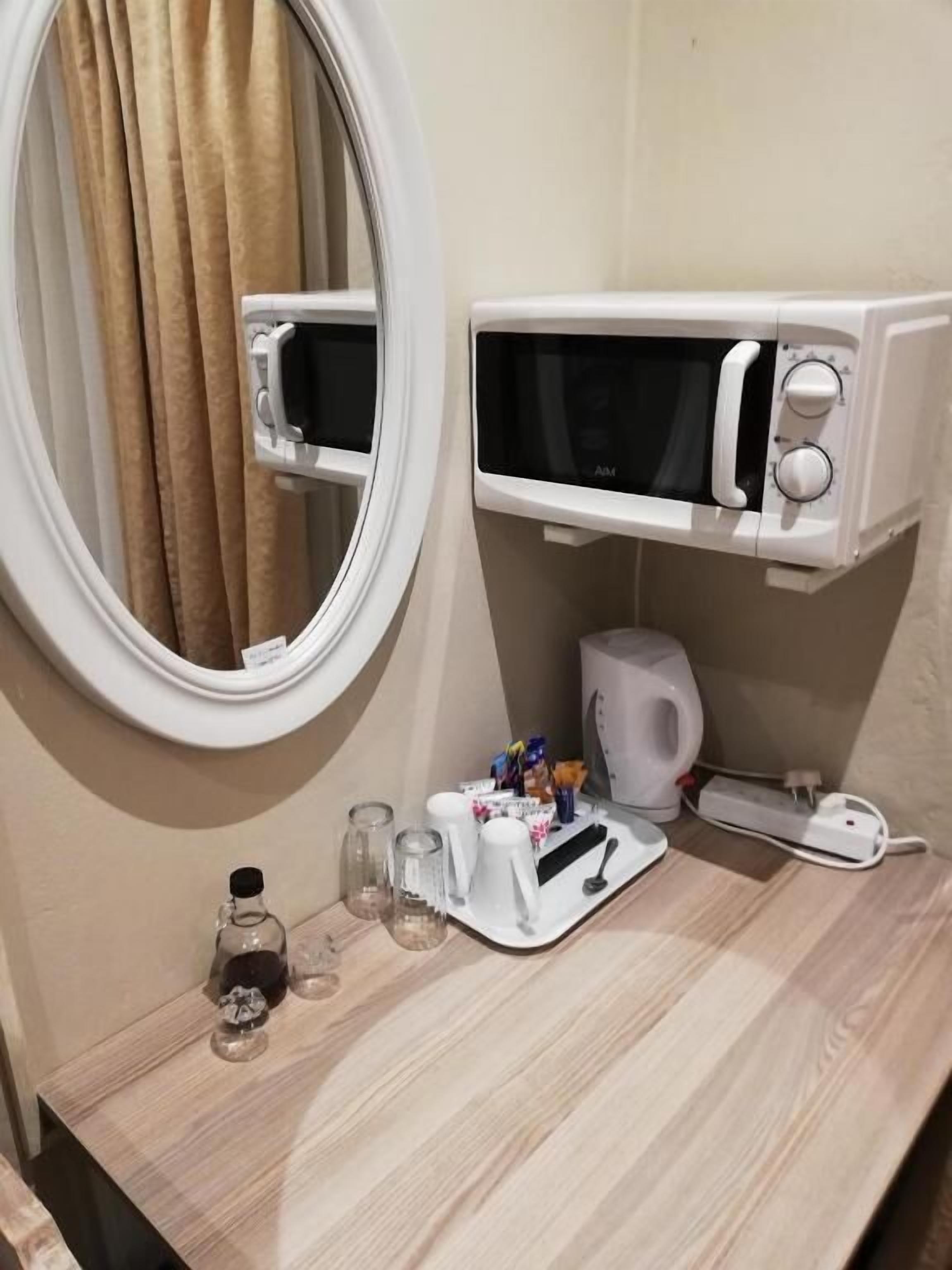 A bathroom with a round mirror, a microwave, a kettle, and a tray with toiletries.