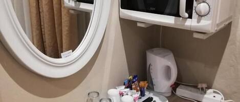 A bathroom with a round mirror, a microwave, a kettle, and a tray with toiletries.
