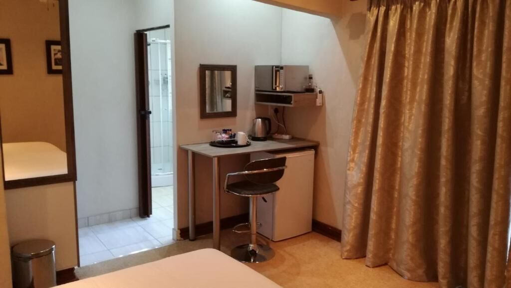 Een hotelkamer met een bed, een bureau met stoel, een spiegel, een kleine kitchenette en een gordijn.