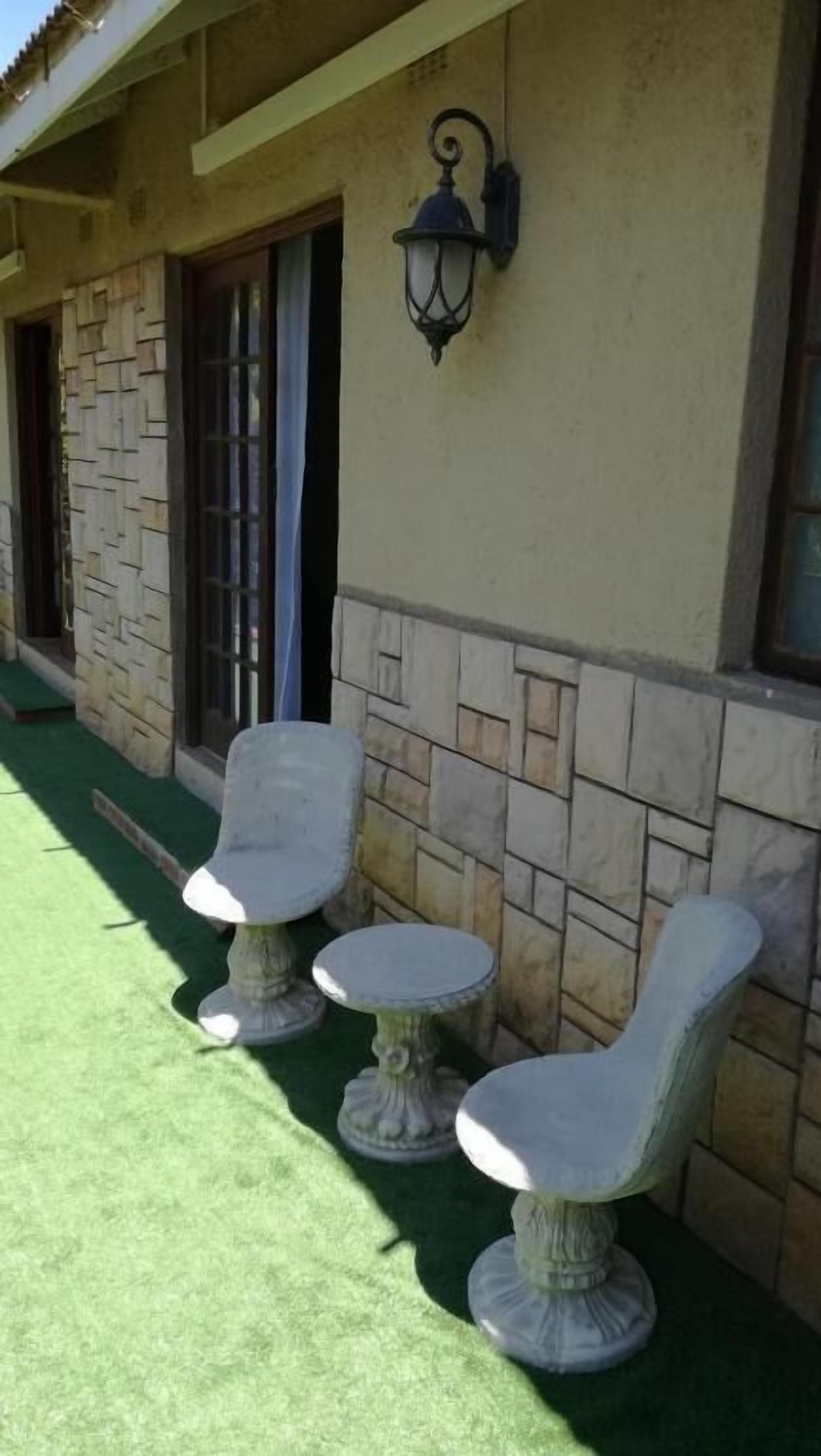 A building with a stone facade, a green artificial lawn, and three outdoor tables with chairs.