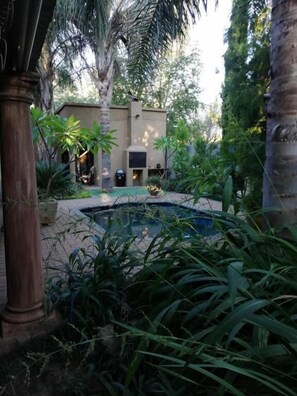 Un patio con piscina, palmeras y un edificio con puerta y ventanas.