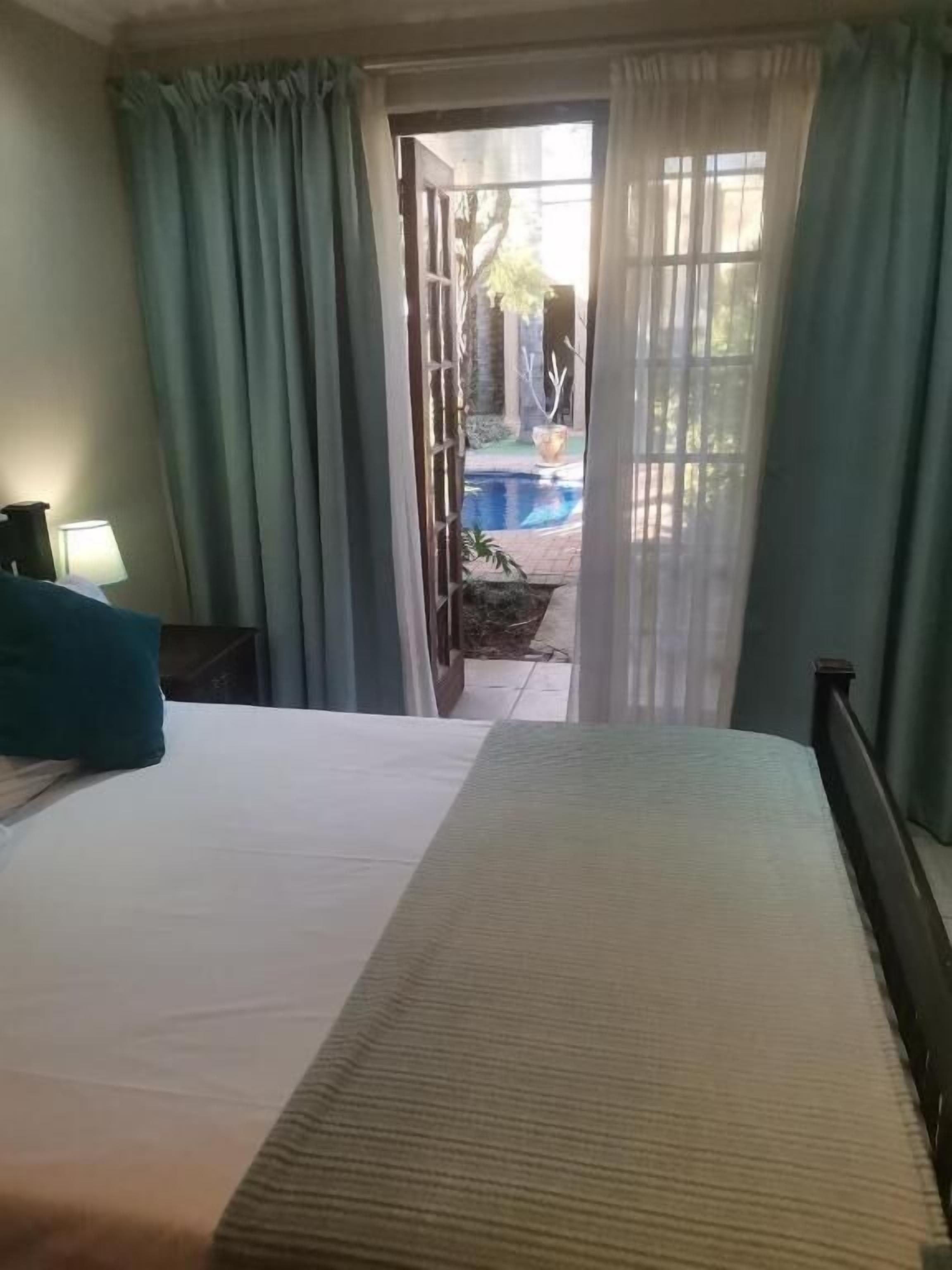 A hotel room with a bed, a nightstand, a lamp, and a view of a swimming pool through an open door.