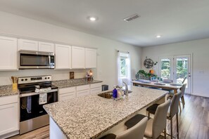 A modern kitchen with white cabinetry, a granite countertop, stainless steel appliances, and a dining area with a large island. - Work & Play! Peaceful Extended Stay in Hoschton (Hoschton)