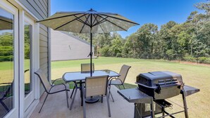 Um pátio com mesa, cadeiras, churrasqueira e um grande guarda-sol.