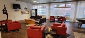 A modern lounge with red sofas, a pool table, a bookshelf, and a TV.