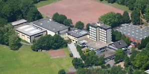 An aerial view of a school building with multiple buildings, a large sports field, and surrounding greenery.