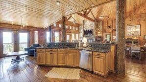 A spacious kitchen with wooden cabinets, a granite countertop, and a stone fireplace. - Hot Tub + Fire Pit: Spacious Waynesville Escape! (Waynesville)
