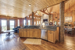 A spacious kitchen with wooden cabinets, a granite countertop, and a stone fireplace. - Hot Tub + Fire Pit: Spacious Waynesville Escape! (Waynesville)