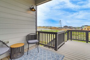 Eine Holzterrasse mit Geländer, ein Korbstuhl, ein kleiner runder Tisch und ein blau gemustertes Teppich.