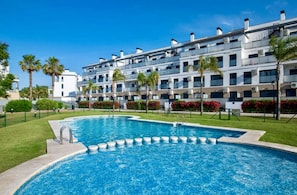 Ein modernes Hotel mit Schwimmbad, Palmen und einem gepflegten Rasen.