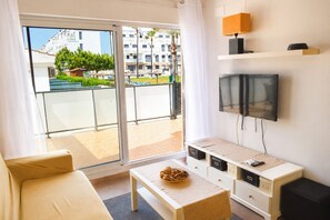 Ein modernes Wohnzimmer mit einer Couch, einem Tisch mit Obstschale, einem Fernseher und einer Glastür zum Balkon.