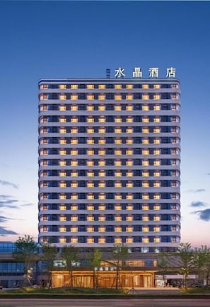 A high-rise hotel with multiple floors, a well-lit entrance, and a clear sky.