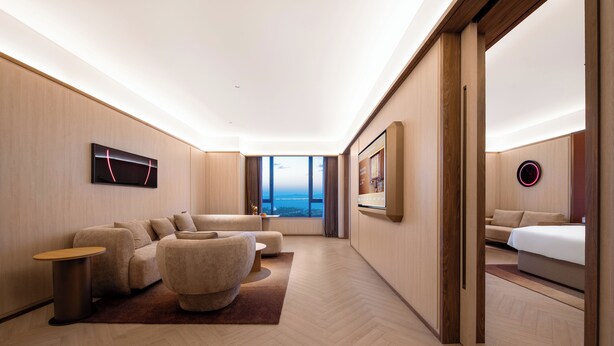 Una habitación de hotel moderna con un ventanal grande, un sofá, una cama y un televisor.