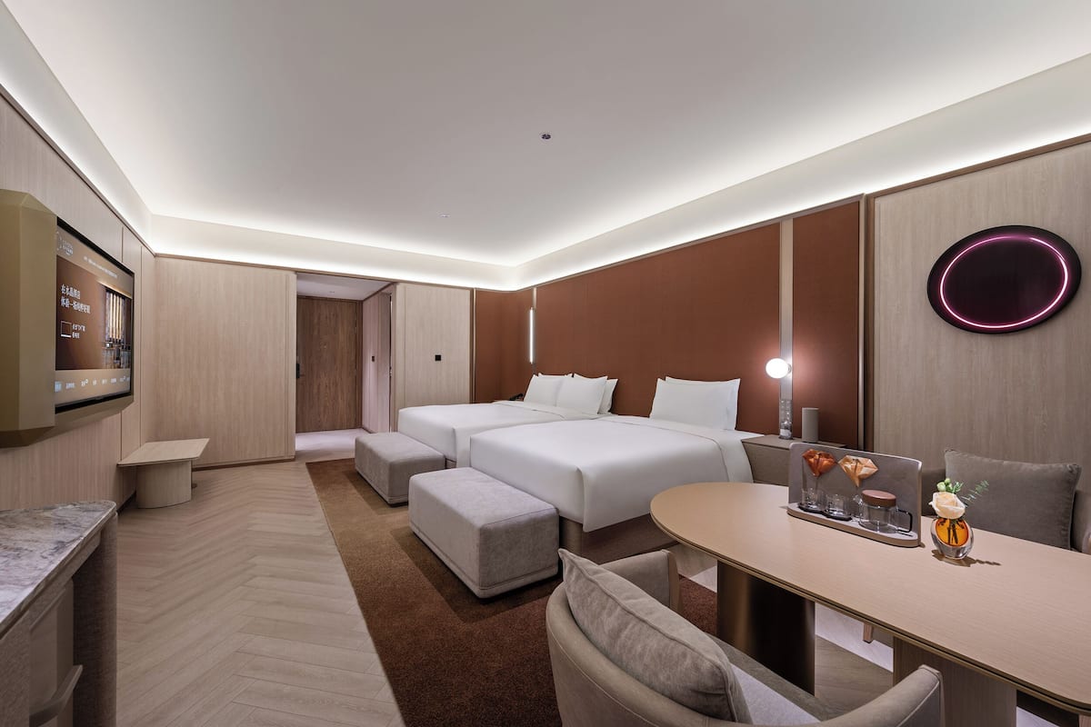 A modern hotel room with a bed, two bedside tables, a desk, and a seating area.