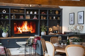 A cozy living room with a fireplace, a bookshelf, and a dining area. - Luxury Rural Barn with Hot Tub for Family & Friends (Walton)