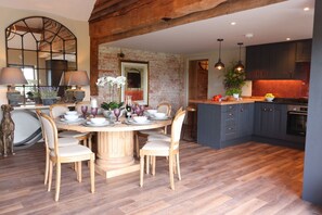 A dining area with a round wooden table, chairs, and a brick wall. - Luxury Rural Barn with Hot Tub for Family & Friends (Walton)