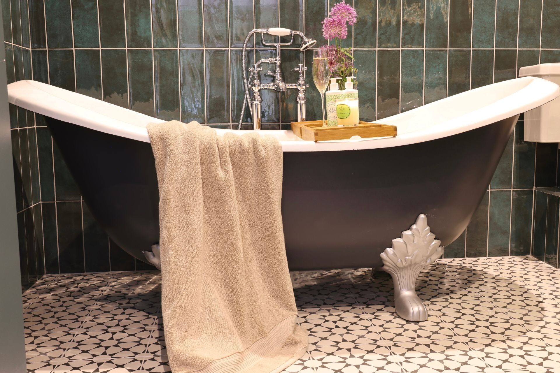 Una vasca da bagno con un asciugamano, un bicchiere di champagne e articoli da toilette sul bordo.