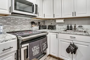 Una cocina con armarios blancos, microondas, estufa y lavamanos.